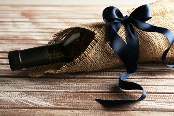 Wine bottle wrapped in burlap cloth on wooden planks background