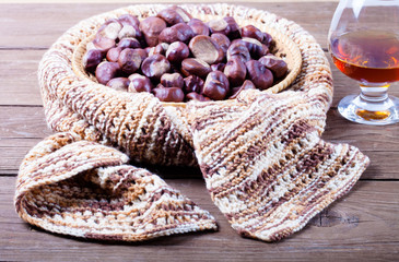 Many chestnuts in a knitted scarf and cognac in a glass on old w