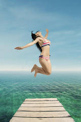 Fototapeta na wymiar Excited woman in swimsuit jumps at pier