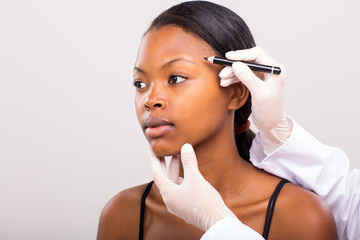 doctor drawing correcting lines on african girl face