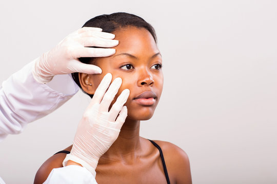 dermatologist checking young african american woman face skin