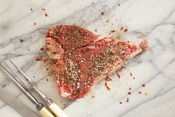 beef steak t-bone with vintage meat fork on marble backdrop