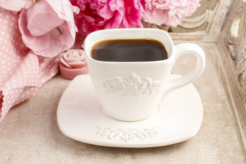 Cup of coffee and beautiful pink peonies in the background