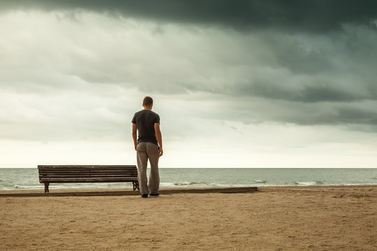 Man goes to the sea near old wooden empty bench