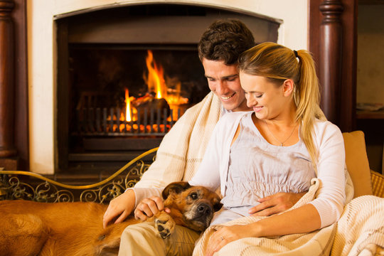 Young Couple Sitting By Fireplace With Their Pet Dog