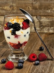 Mixed berry, granola and yogurt parfait on wood with spoon