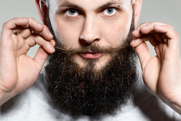 man with beard adjusting his mustaches