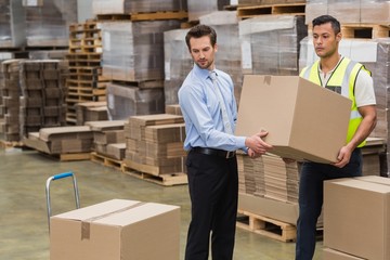 Warehouse worker and manager carrying a box together