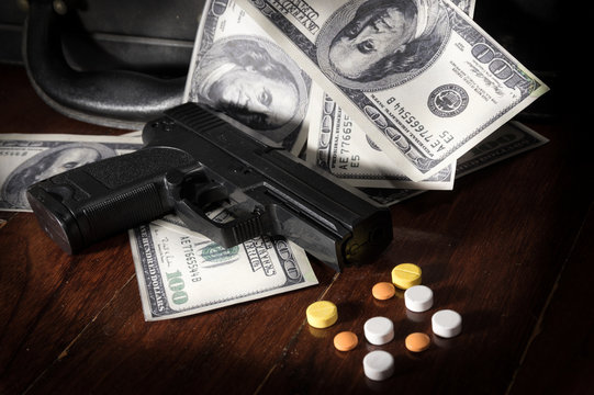 Gun and drug pills on dollar bills.