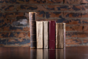 Vintage old books on a wooden table top  against a brick wall