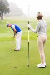 Lady golfer holding flag for partner putting ball