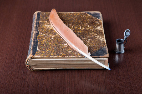 Old book, quill and black ink on wooden desk
