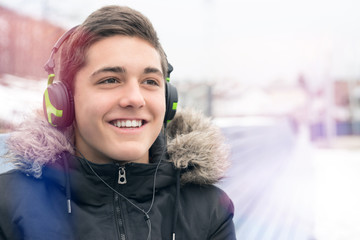Young smiling boy listening music outdoors in winter