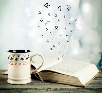 Fototapeta Open book with flying letters on table on bright background