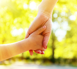 Mom and daughter hands on sunny nature background