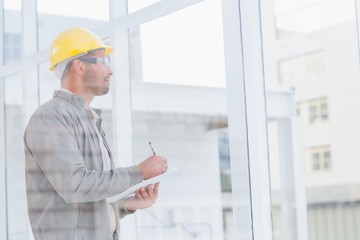 Architect writing on clipboard while looking through window