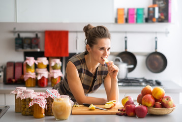 Young housewife standing near jars with fruits jam 