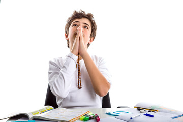 boy prays  with a rosary with clasped hands while doing homework