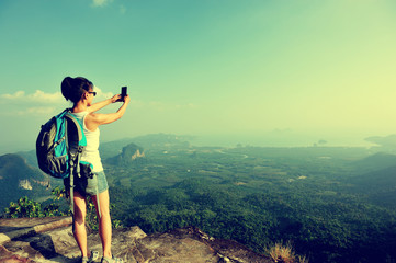 woman hiker taking photo with smart phone at mountain peak 