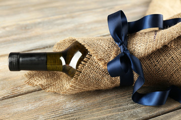 Wine bottle wrapped in burlap cloth on wooden planks background