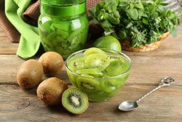 Tasty kiwi jam in glass bowl on wooden background