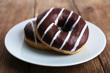 Delicious donuts with icing on plate on wooden background