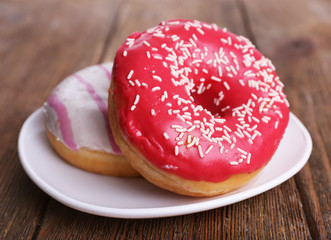 Delicious donuts with icing on plate on wooden background