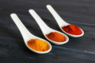 Different kinds of spices in spoons on wooden background
