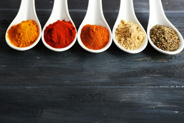Different kinds of spices in spoons on wooden background