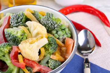 Frozen vegetables in bowl on napkin, on wooden table background