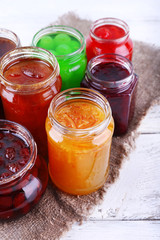 Homemade jars of fruits jam on color wooden planks background