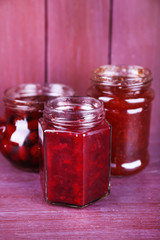 Homemade jars of fruits jam on color wooden background