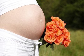 Pregnant woman outdoor with orange tulips in her hands