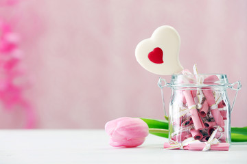 Jar of papers with sweet heart on table on bright background