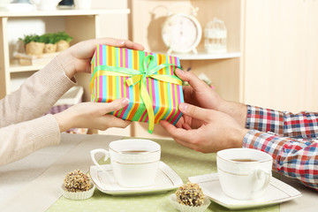Female and male hands with cups of tea and gift box