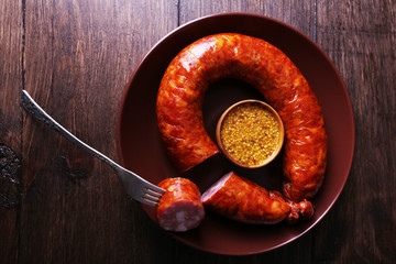 Smoked sausage with mustard on plate on wooden table background
