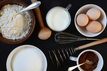 Baking ingredients on a table: eggs, flour, milk, sugar, cacao.