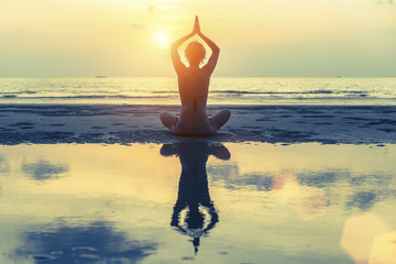 Silhouette of a young girl practicing yoga on the during sunset.