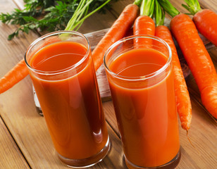 glasses of carrot juice and fresh carrots on a wooden table
