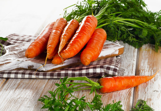 Bunch of fresh carrots with green leaves on  wooden background