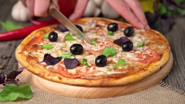 Pizza margherita with mozzarella, olives is been cutted by man