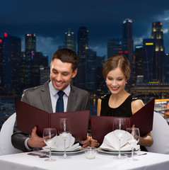 smiling couple with menus at restaurant