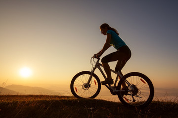 Fototapeta na wymiar Biker-girl at the sunset on mountains