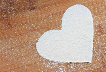 Heart from flour on wooden plank background