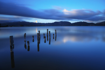 Wooden pier or jetty remains on a blue lake sunset and sky refle