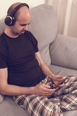 Obraz premium Man in pajamas sitting in the sofa and listening to the music