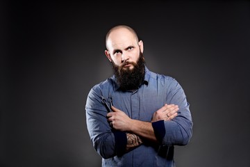 Bald man with a beard holding a pair of scissors.