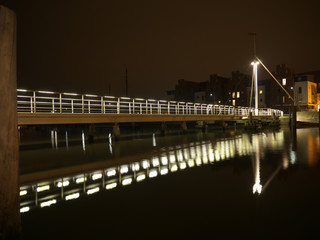 Beleuchtete lange Brücke mit Geländer und Spiegelungen bei Nacht im Greifswalder Hafen
