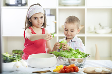 Little brother and sister preparing salad in the kitchen