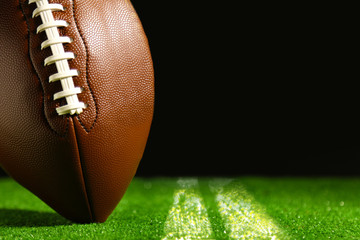 American football on green grass on black background